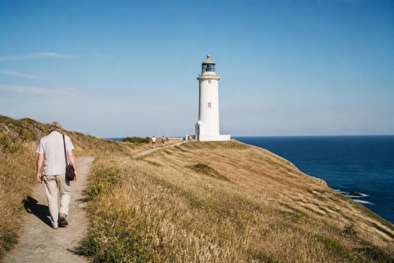 Wandelaar op een kustpad richting een witte vuurtoren op een zonnige kaap
