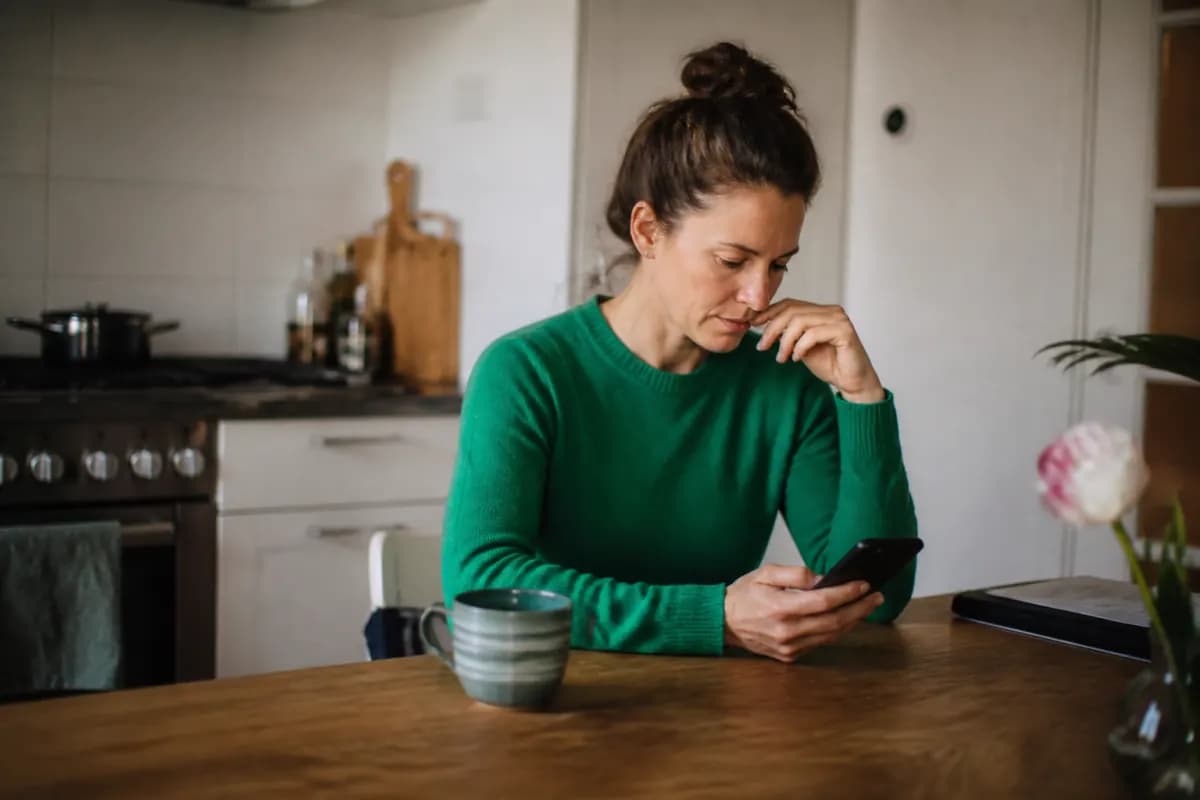 Vrouw vult aan de keukentafel op haar telefoon het assessment in, met een kop koffie naast zich
