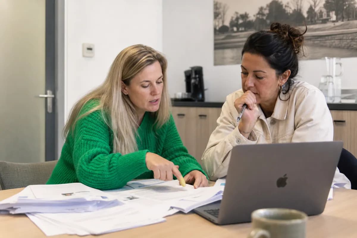 HR-adviseur en teamleider bekijken samen een stapel sollicitaties naast een laptop