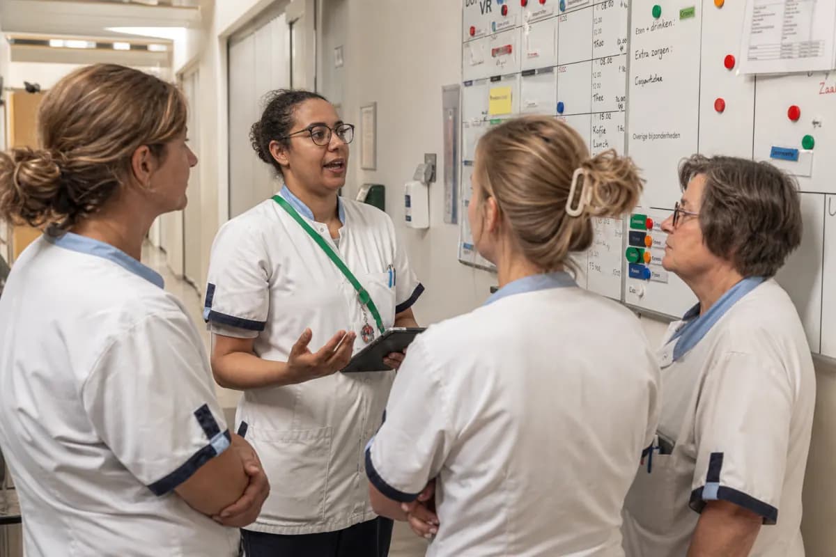Zorgteam in werktenue bij een overdracht voor een planbord op de afdeling