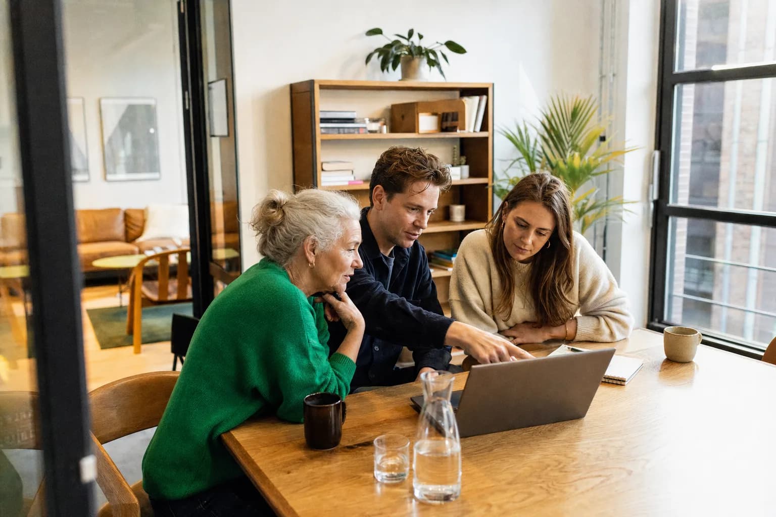 Drie collega's overleggen samen achter een laptop aan een houten tafel